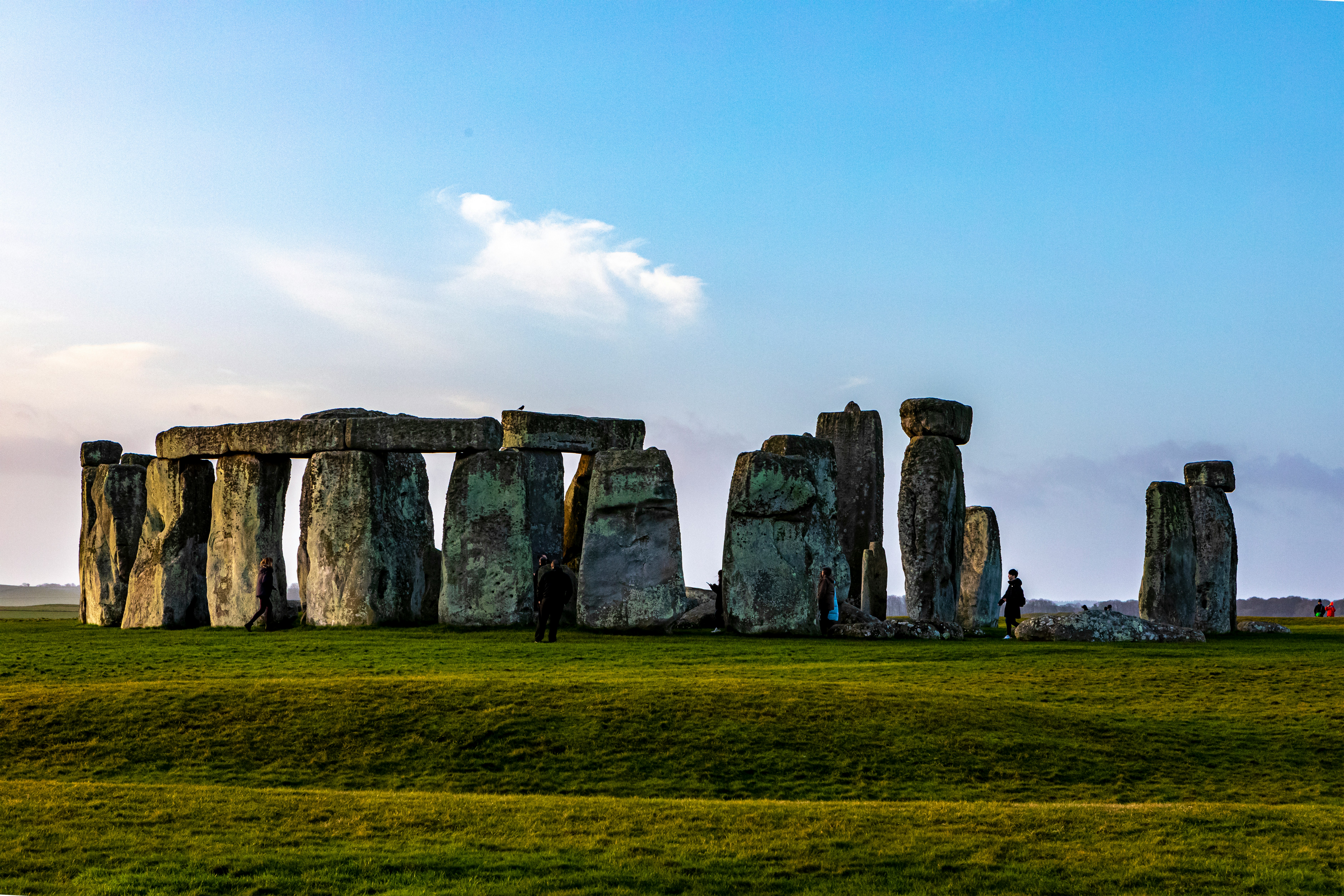Grey rock formation on green grass field under white clouds during daytime.